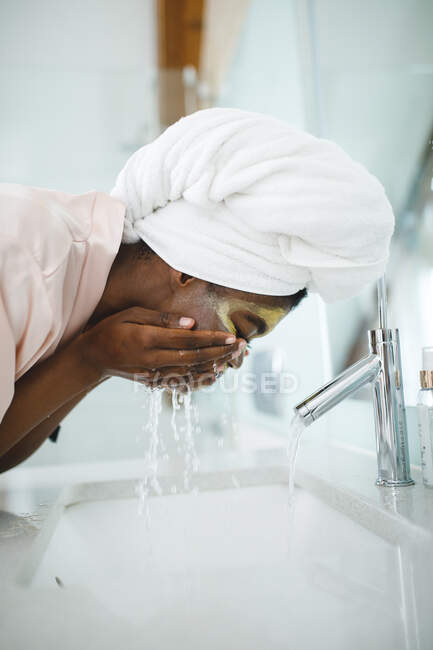 Donna afroamericana in bagno lavarsi via maschera di bellezza. stile di vita domestico, godendo di auto cura del tempo libero a casa. — Foto stock