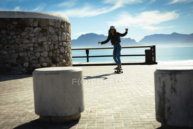 Mixed race woman skateboarding on sunny day by seaside. healthy lifestyle, enjoying leisure time outdoors. — Stock Photo