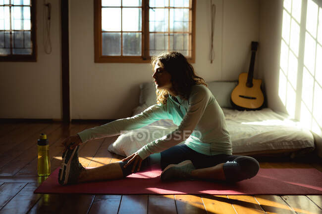 Donna razza mista praticare yoga, che si estende in soggiorno soleggiato. stile di vita sano, godendo del tempo libero a casa. — Foto stock