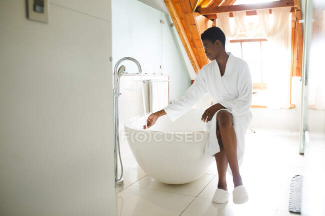 Mujer afroamericana en el baño haciendo un baño. estilo de vida doméstico, disfrutando del tiempo libre de autocuidado en casa. - foto de stock