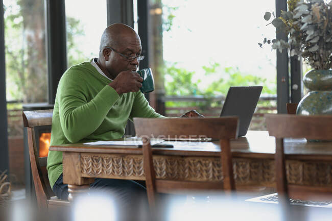 Ein älterer afrikanisch-amerikanischer Mann sitzt und arbeitet am Laptop im modernen Wohnzimmer. Lebensstil im Ruhestand, Zeit allein zu Hause verbringen. — Stockfoto