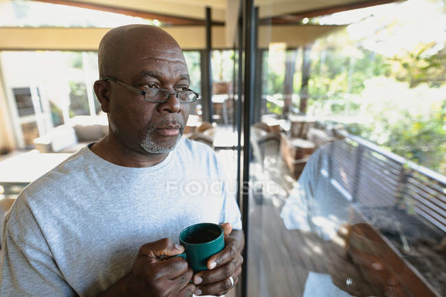 Nachdenklicher älterer afrikanisch-amerikanischer Mann, der eine Tasse Kaffee einschenkt und zum Fenster blickt. Lebensstil im Ruhestand, Zeit allein zu Hause verbringen. — Stockfoto