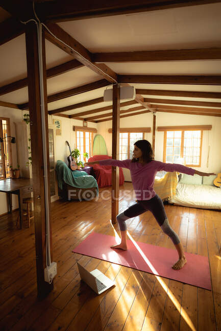 Femme de race mixte pratiquant le yoga dans le salon ensoleillé. mode de vie sain, profiter de loisirs à la maison. — Photo de stock