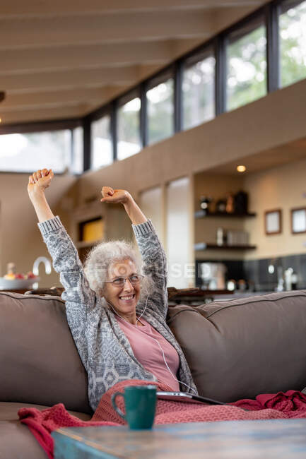 Felice donna caucasica anziani seduti sul divano e utilizzando tablet nel moderno soggiorno. stile di vita di pensione, trascorrere del tempo da solo a casa. — Foto stock