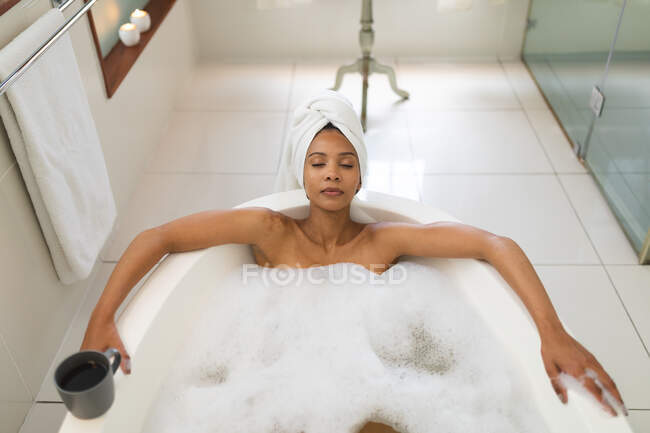 Gemischte Rassenfrau im Badezimmer mit Badewanne, entspannend mit geschlossenen Augen. häuslicher Lebensstil, selbstgepflegte Freizeit zu Hause genießen. — Stockfoto