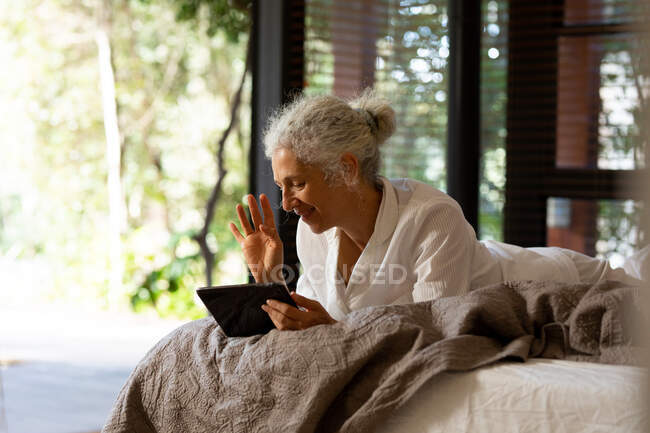 Senior caucasian woman lying on the bad and making video call. retirement lifestyle, spending time alone at home. — Stock Photo