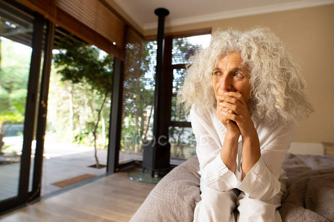 Pensativa mujer caucásica mayor sentada en el mal y pensando. estilo de vida de jubilación, pasar tiempo solo en casa. - foto de stock