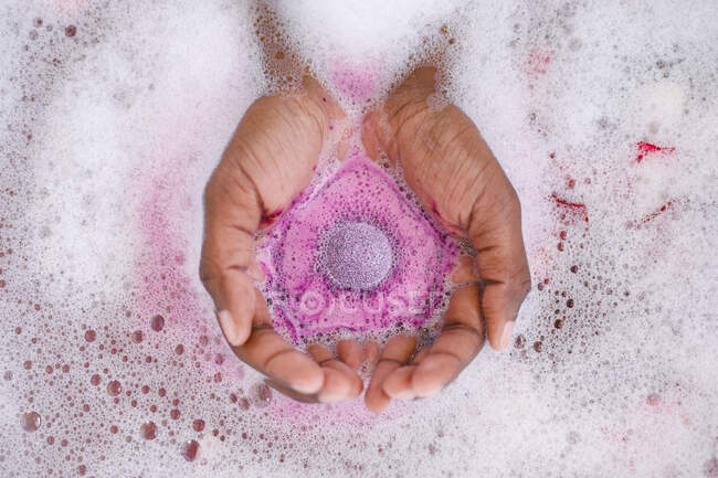 Закрыть руки женщины, принимающей ванну, держащей в руках шипящую бомбу для ванны. домашний образ жизни, наслаждаясь отдыхом на дому. — стоковое фото