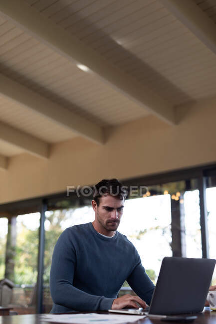 Kaukasier sitzt am Tisch und arbeitet mit Laptop. Arbeiten zu Hause in moderner Wohnung. — Stockfoto
