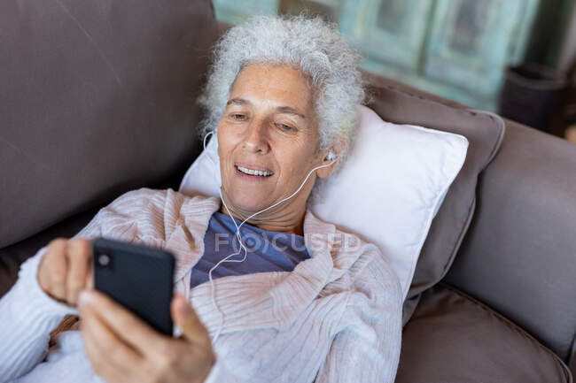 Senior caucasian woman laying and using smartphone in the modern living room. retirement lifestyle, spending time alone at home. — Stock Photo