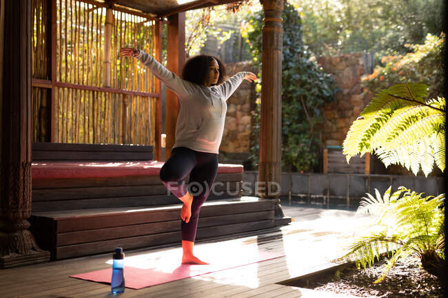 Donna di razza mista che indossa abbigliamento sportivo e pratica yoga su tappetino yoga. trascorrere del tempo libero a casa. — Foto stock