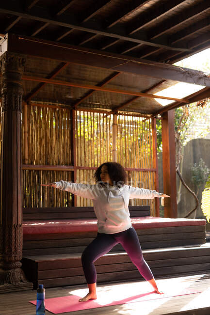 Смешанная расовая женщина носит спортивную одежду и практикует йогу на коврике для йоги. проводить свободное время дома. — стоковое фото