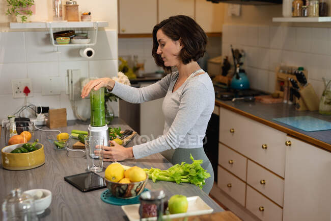 Caucasian woman standing in kitchen, preparing health drink. domestic lifestyle, enjoying leisure time at home. — Stock Photo