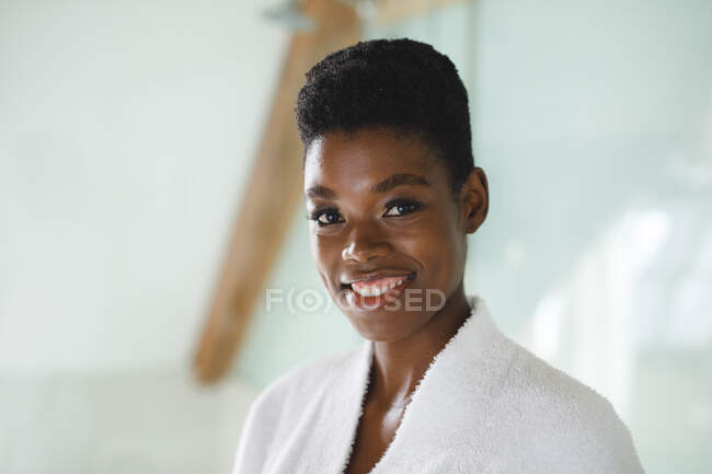 Retrato de mulher afro-americana sorridente no banheiro usando roupão de banho. estilo de vida doméstico, desfrutando de tempo de lazer auto-cuidado em casa. — Fotografia de Stock