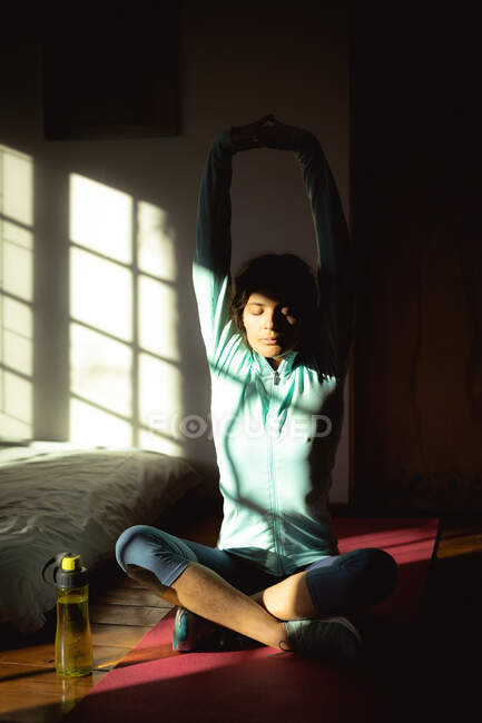 Donna razza mista praticare yoga, che si estende in soggiorno soleggiato. stile di vita sano, godendo del tempo libero a casa. — Foto stock