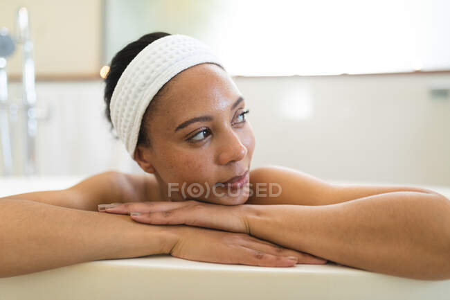 Mujer de raza mixta en baño relajante en bañera. estilo de vida doméstico, disfrutando del tiempo libre de autocuidado en casa. - foto de stock