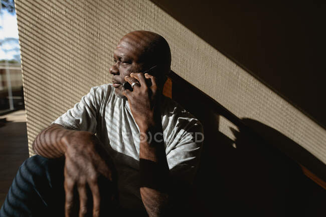 Hombre afroamericano mayor sentado en las escaleras y hablando en el teléfono inteligente. estilo de vida de jubilación, pasar tiempo solo en casa. - foto de stock