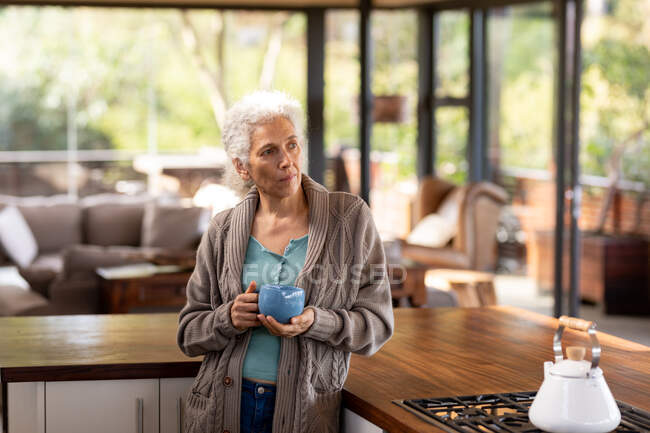 Mulher caucasiana sênior na cozinha de pé e bebendo café. estilo de vida aposentadoria, passar o tempo sozinho em casa. — Fotografia de Stock
