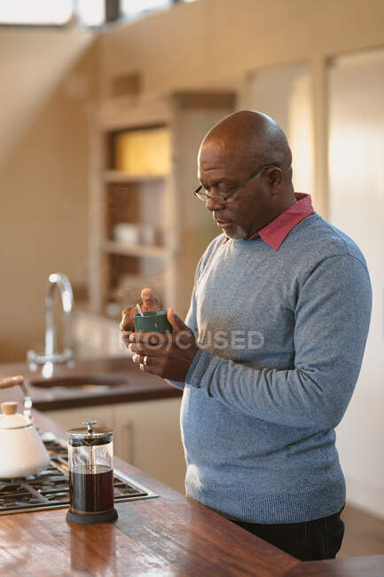 Homem americano africano sênior em pé na cozinha moderna bebendo um café. estilo de vida aposentadoria, passar o tempo sozinho em casa. — Fotografia de Stock