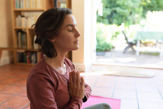 Кавказька жінка у вітальні, практикує йогу, медитує. Домашнє життя, дозвілля вдома. — стокове фото