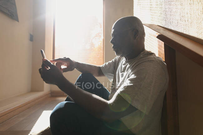 Homem americano africano sênior pensativo situado nas escadas ensolaradas e usando smartphone. estilo de vida aposentadoria, passar o tempo sozinho em casa. — Fotografia de Stock