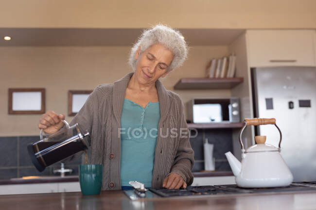 Расслабляющая пожилая кавказка на кухне варит кофе. пенсионного образа жизни, проводить время в одиночестве на дому. — стоковое фото