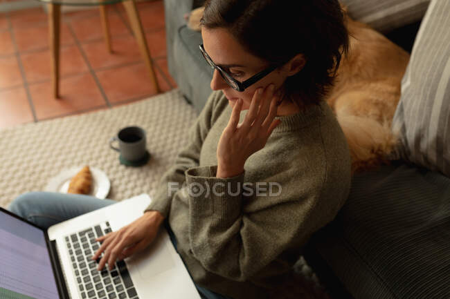 Donna caucasica in soggiorno con il suo cane domestico, seduta sul pavimento, che lavora con il computer portatile. stile di vita domestico, godendo del tempo libero a casa. — Foto stock