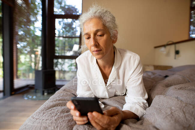 Старша біла жінка лежить на поганому і використовує планшет. пенсійний спосіб життя, проводити час наодинці вдома . — стокове фото