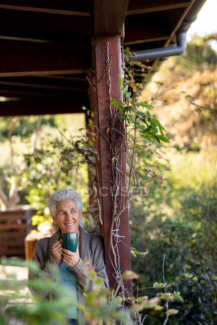 Rilassante donna caucasica anziana sul balcone in piedi e bere caffè. stile di vita di pensione, trascorrere del tempo da solo a casa. — Foto stock