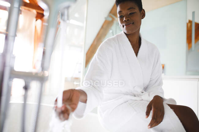 Uma mulher afro-americana sorridente na casa de banho a tomar banho. estilo de vida doméstico, desfrutando de tempo de lazer auto-cuidado em casa. — Fotografia de Stock