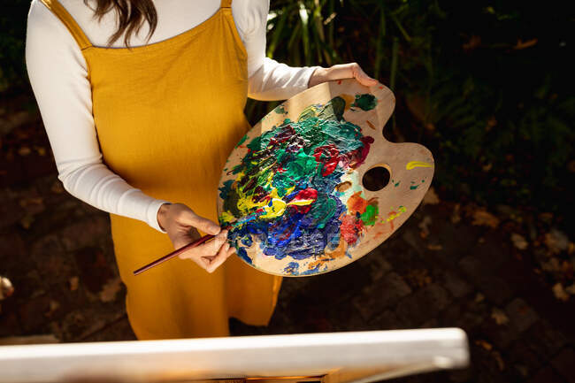 Frau im sonnigen Garten und mischt Farbe auf Palette. häuslicher Lebensstil, Freizeit zu Hause genießen. — Stockfoto