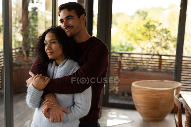 Happy diverse couple in living room together embracing and smiling. spending time off at home in modern apartment. — Stock Photo
