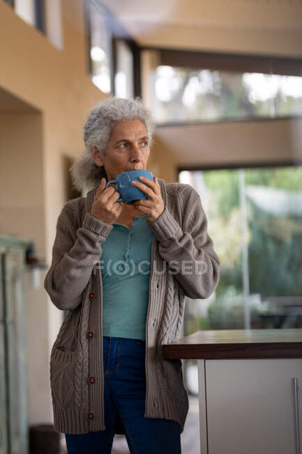 Eine ältere kaukasische Frau steht in der Küche und trinkt Kaffee. Lebensstil im Ruhestand, Zeit allein zu Hause verbringen. — Stockfoto
