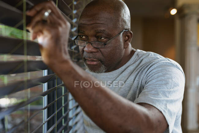 Um homem afro-americano atencioso a olhar para a janela. estilo de vida aposentadoria, passar o tempo sozinho em casa. — Fotografia de Stock