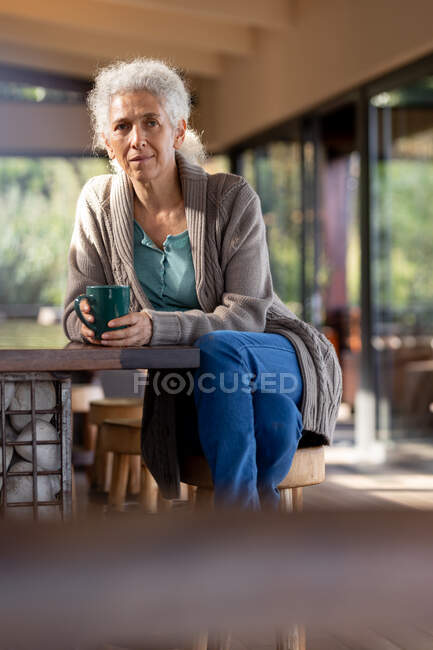 Расслабляющая пожилая кавказка на кухне сидит и пьет кофе. пенсионного образа жизни, проводить время в одиночестве на дому. — стоковое фото