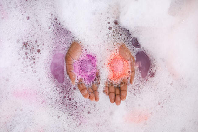 Primer plano de las manos de una mujer afroamericana tomando un baño de mimar, sosteniendo bombas de baño fizzing. estilo de vida doméstico, disfrutando del tiempo libre de autocuidado en casa. - foto de stock