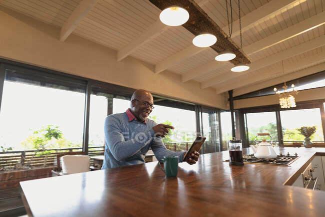 Счастливый старший африканский американец сидит на современной кухне и делает видеозвонок. пенсионного образа жизни, проводить время в одиночестве на дому. — стоковое фото