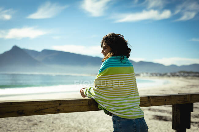 Mujer de raza mixta de pie en un día soleado junto al mar. estilo de vida saludable, disfrutar del tiempo libre al aire libre. - foto de stock