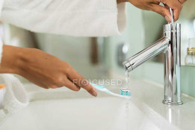 Woman in bathroom holding toothbrush under running water. domestic lifestyle, enjoying self care leisure time at home. — Stock Photo