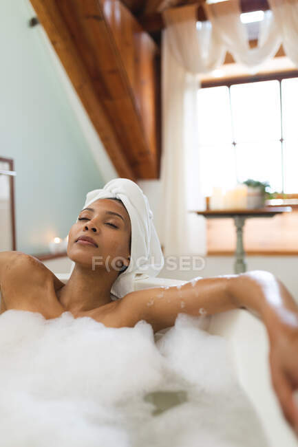 Femme de race mixte dans la salle de bain ayant une baignoire, relaxant avec les yeux fermés. mode de vie domestique, profiter de loisirs d'auto-soins à la maison. — Photo de stock