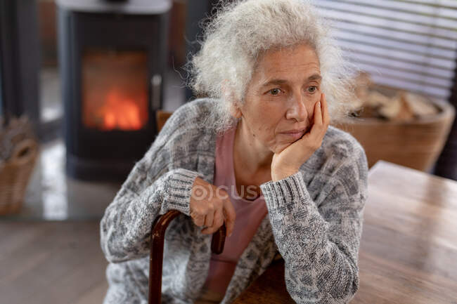 Traurige ältere kaukasische Frau, die in der Küche sitzt und sich auf einen Gehstock stützt. Lebensstil im Ruhestand, Zeit allein zu Hause verbringen. — Stockfoto