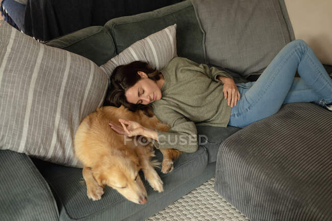 Sorridente donna caucasica in soggiorno, sdraiata sul divano con il suo cane da compagnia. stile di vita domestico, godendo del tempo libero a casa. — Foto stock