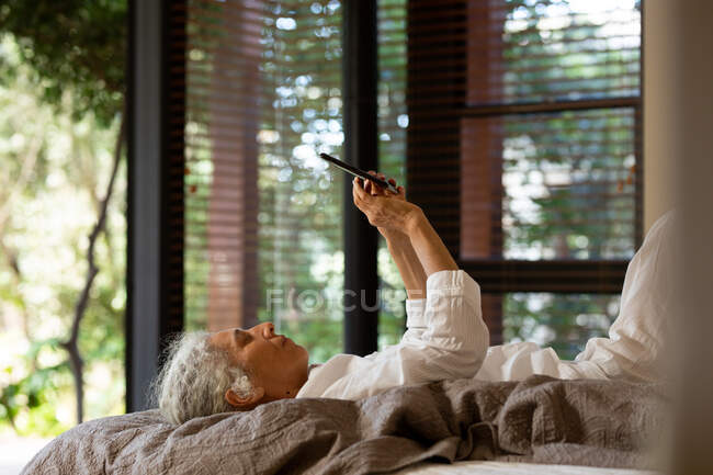 Femme caucasienne aînée allongée sur la mauvaise et utilisant une tablette. mode de vie à la retraite, passer du temps seul à la maison. — Photo de stock