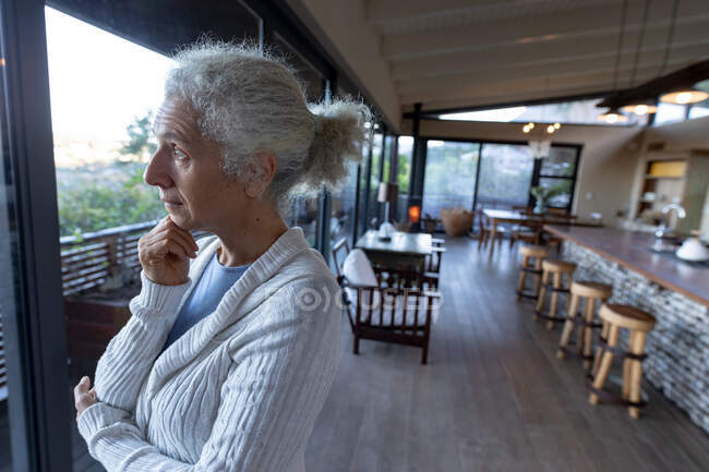 Pensativo anciano mujer caucásica en la cocina de pie y pensando. estilo de vida de jubilación, pasar tiempo solo en casa. - foto de stock