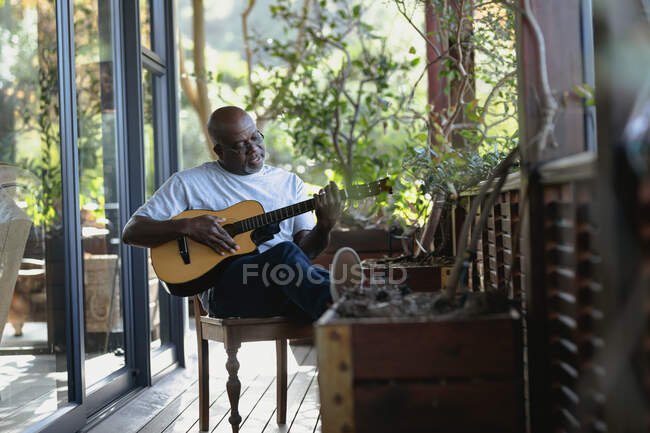 Relaxando o homem afro-americano sênior na varanda ensolarada tocando guitarra. estilo de vida aposentadoria, passar o tempo sozinho em casa. — Fotografia de Stock