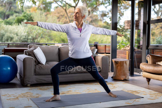 Mulher caucasiana sênior na sala de estar se exercitando, sentada no chão. estilo de vida aposentadoria, passar o tempo sozinho em casa. — Fotografia de Stock