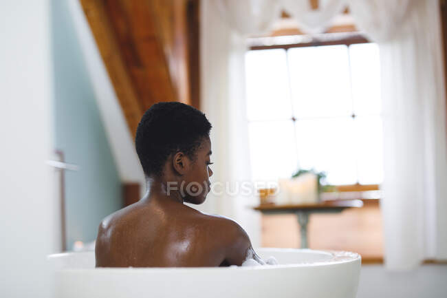 Усміхнена афро-американська жінка у ванній кімнаті, відпочиває у ванній кімнаті. Домашній спосіб життя, дозвілля для себе вдома. — стокове фото
