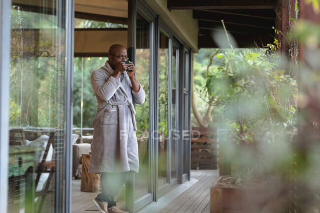 Relajante hombre afroamericano senior en el balcón soleado bebiendo café. estilo de vida de jubilación, pasar tiempo solo en casa. - foto de stock