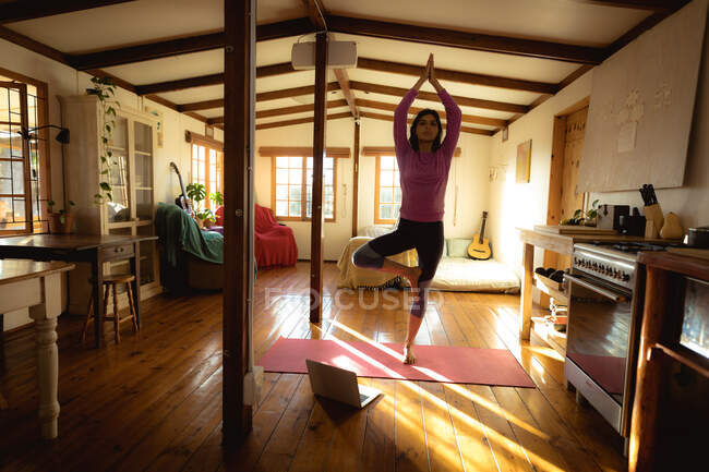 Змішана расова жінка практикує йогу в сонячній вітальні. Здоровий спосіб життя, дозвілля вдома. — стокове фото