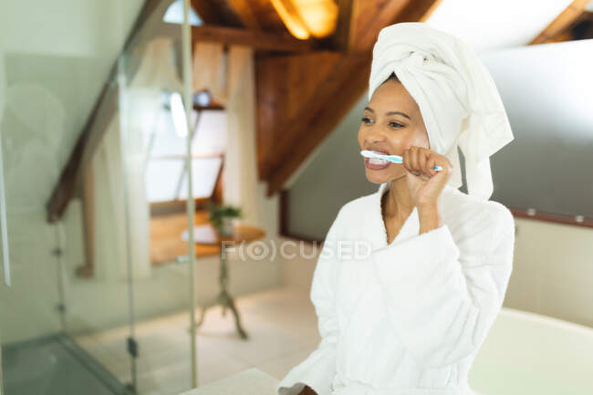 3mixed race woman in bathroom holding toothbrush brushing her teeth. domestic lifestyle, enjoying self care leisure time at home. — Stock Photo